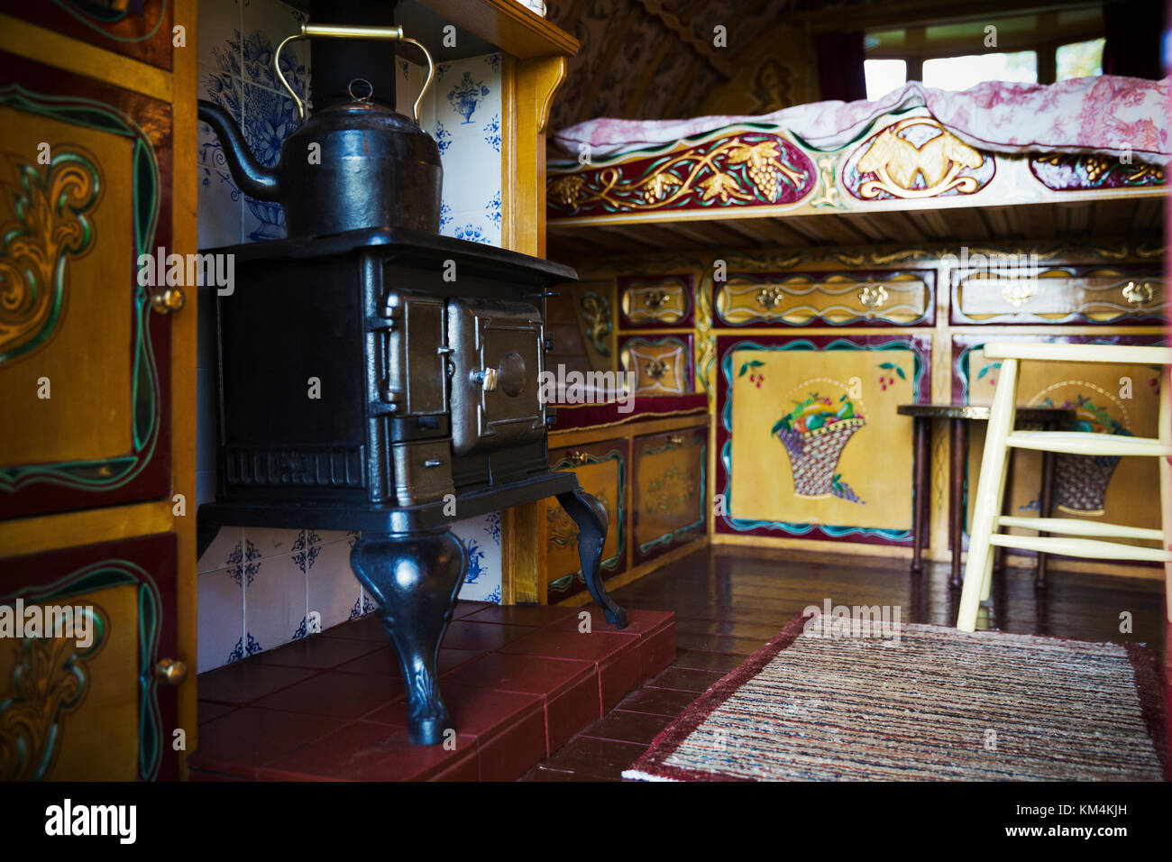 A cast iron stove with large metal kettle, a mantlepiece and storage cupboards and raised bed, the interior of a gypsy caravan, Stock Photo