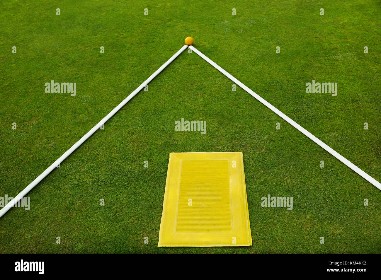 A lawn bowls green edge, a yellow player's mat to stand on and two