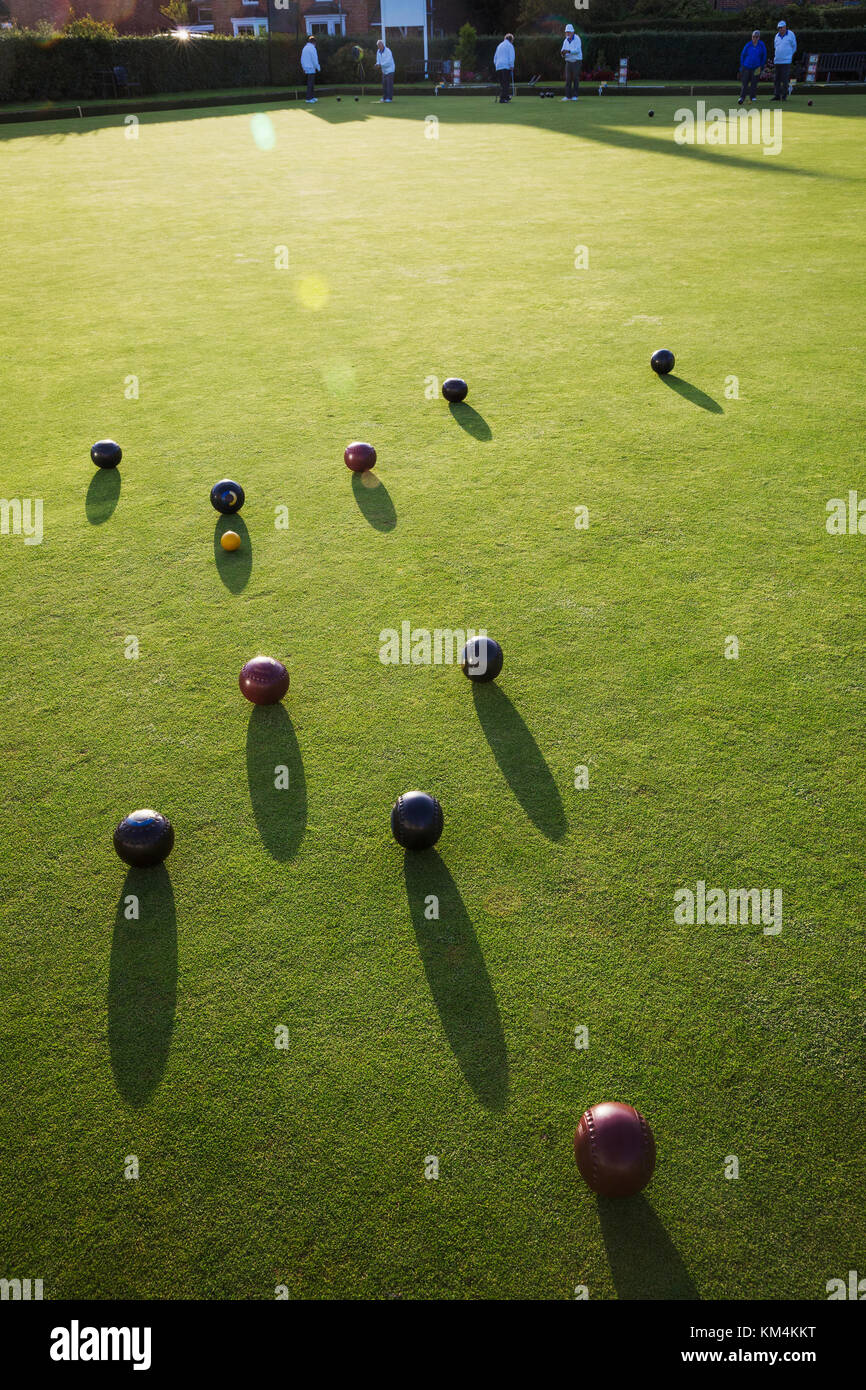 A small yellow target jack ball and a cluster of lawn bowls around it. People in the background. Stock Photo
