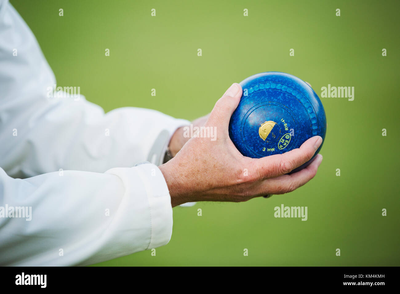A man holding a blue wooden lawn bowls ball in his hands. Stock Photo