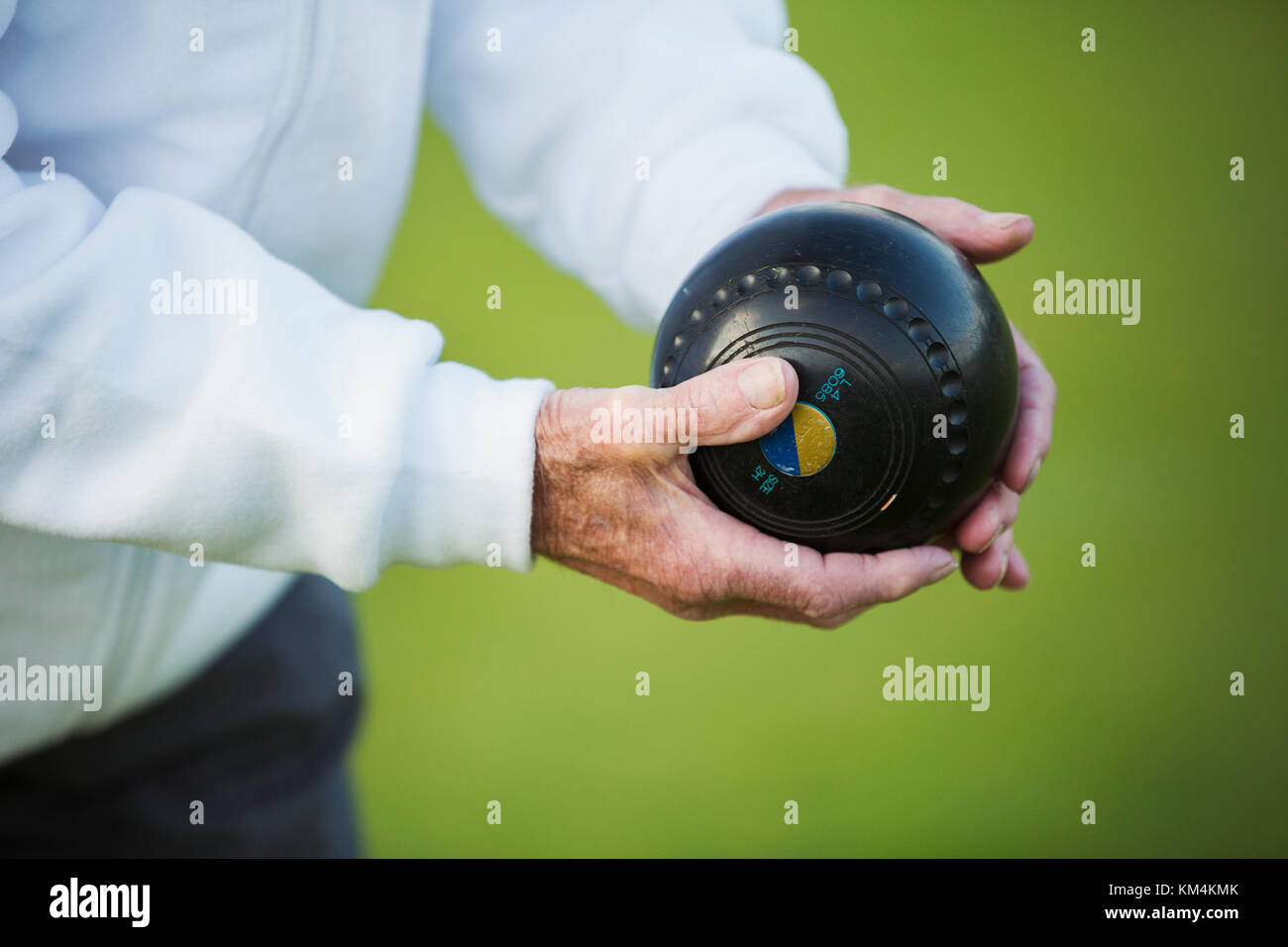 A man holding a black wooden lawn bowls ball in his hands. Notches and grooves in the surface. Stock Photo