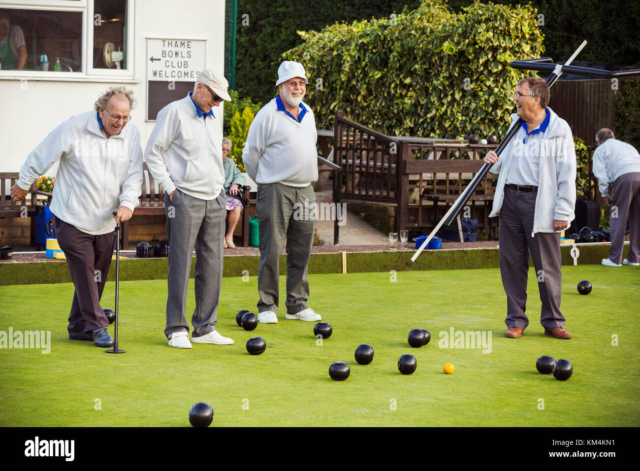 Four men on the lawn bowls green, one wearing an umpire's coat, at an end. Stock Photo