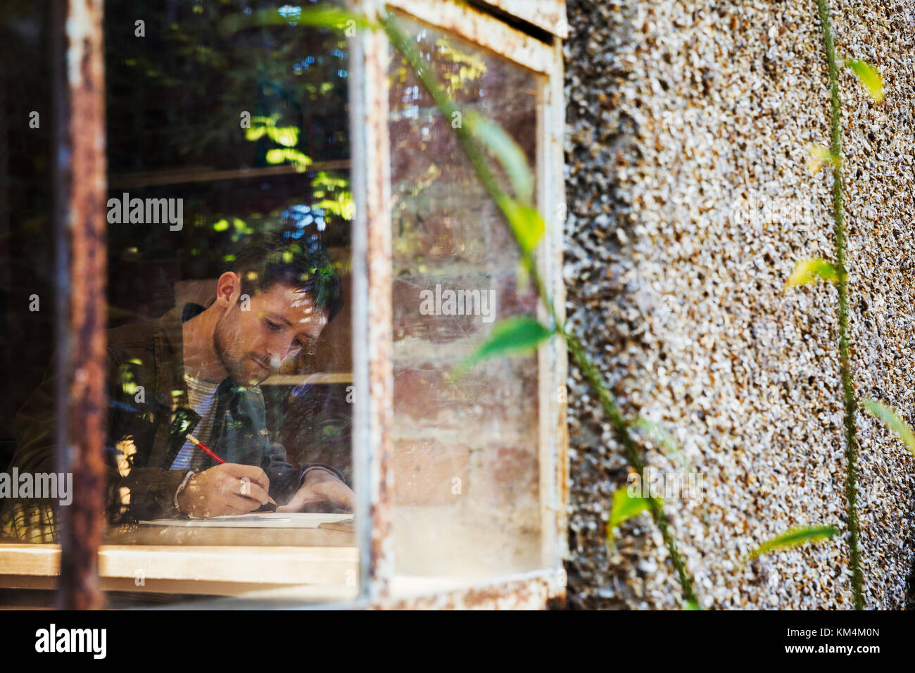 View through a window of a young man drawing in a notebook, a designer at work. Stock Photo