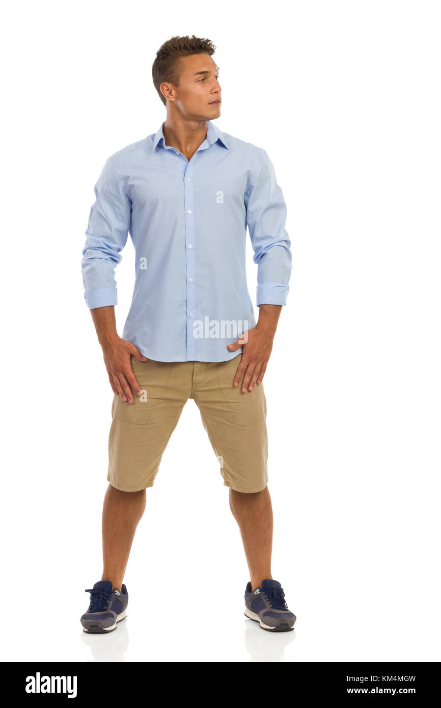 Handsome young man in blue shirt, beige shorts and sneakers standing with  legs apart and looking away. Full length studio shot isolated on white  Stock Photo - Alamy