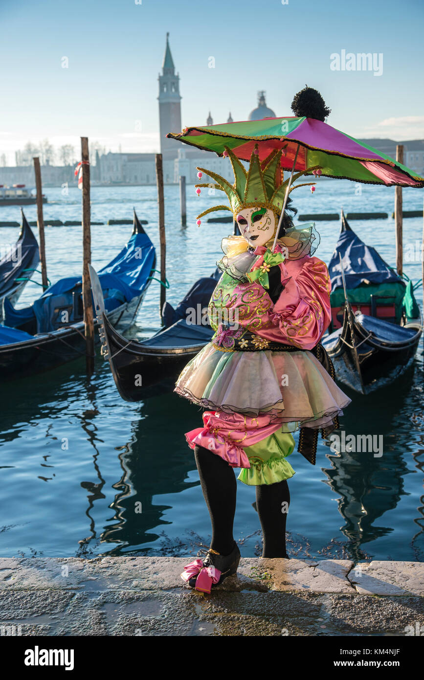 Costumed Venetian standing in front of the gondolas in St. Mark's Square during Carnival in Venice, Italy. Stock Photo