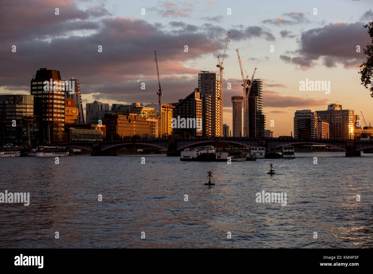 View of the London skyline on the south bank of the River Thames with buildings lit by the setting sun, bridges and the dark river. Stock Photo