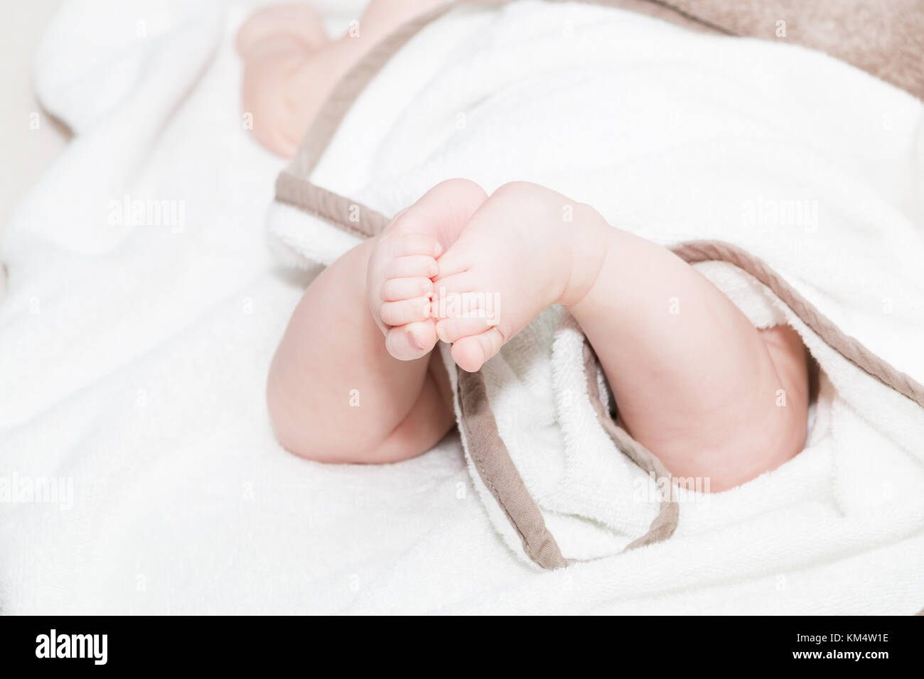 Baby feet under white blanket cover. Close up picture of new born baby feet on a white sheet. Stock Photo