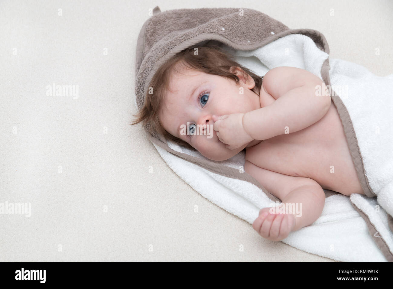 Cute baby girl lying on a white bed blanket and keeps fingers in his