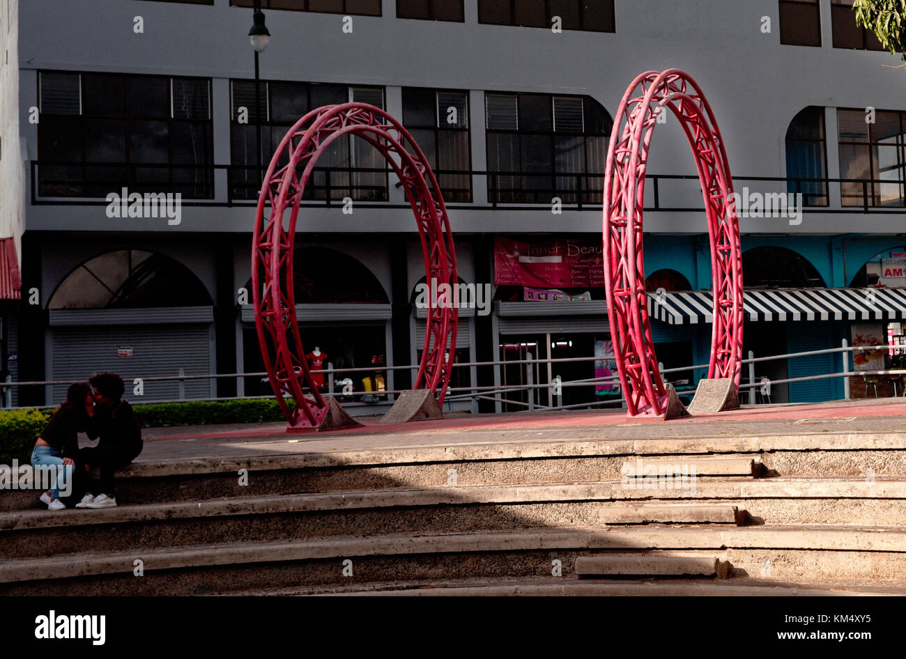 Two red wheels form art in a plaza square, San Jose, Costa Rica behind young couple Stock Photo
