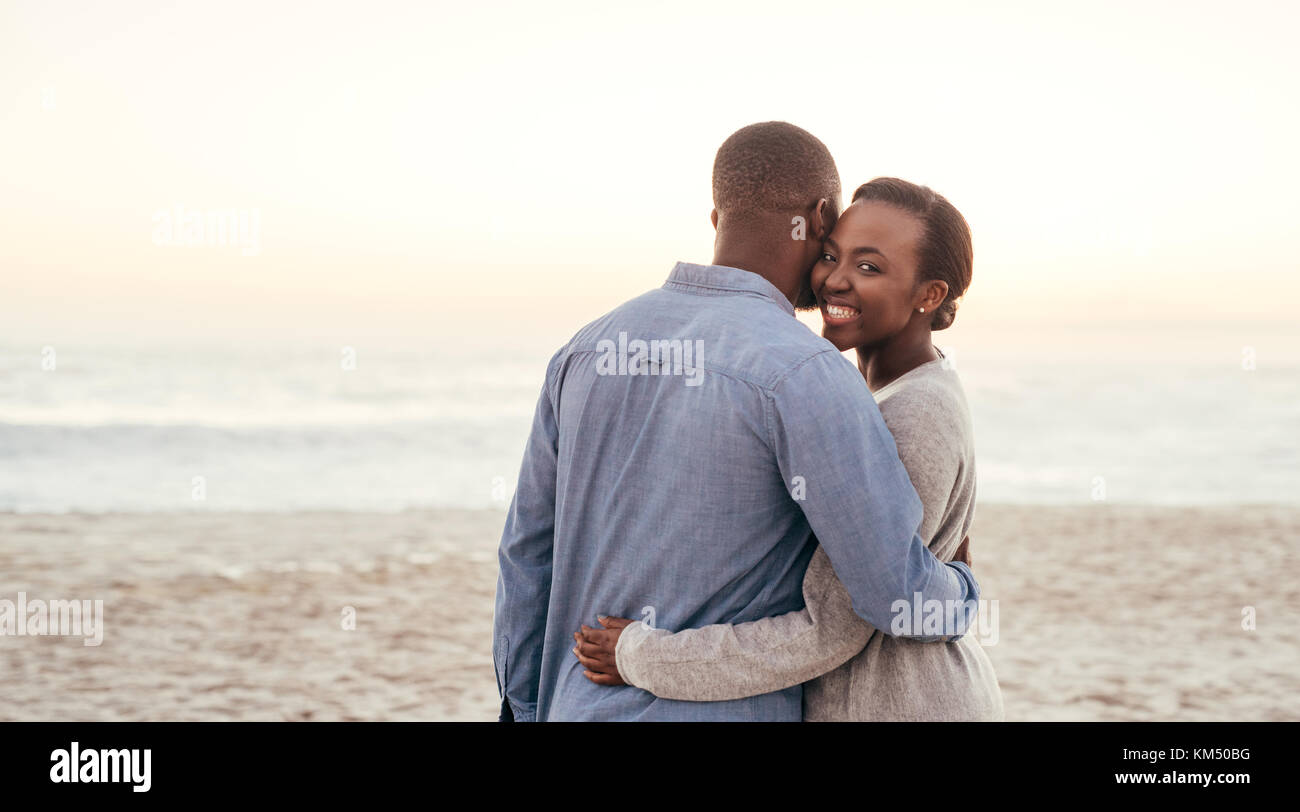 African woman embracing her boyfriend on a beach at sunset Stock Photo