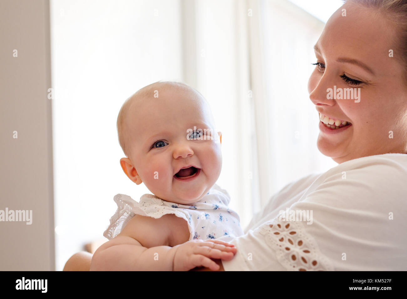 Caring mother holding smiling cute baby girl Stock Photo