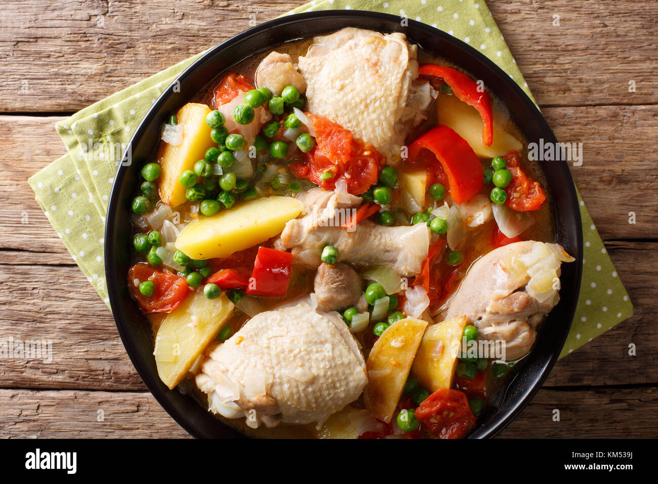 Pieces of chicken stew with potatoes, peppers, tomatoes, peas and onions close-up in a bowl on the table. Horizontal top view from above Stock Photo