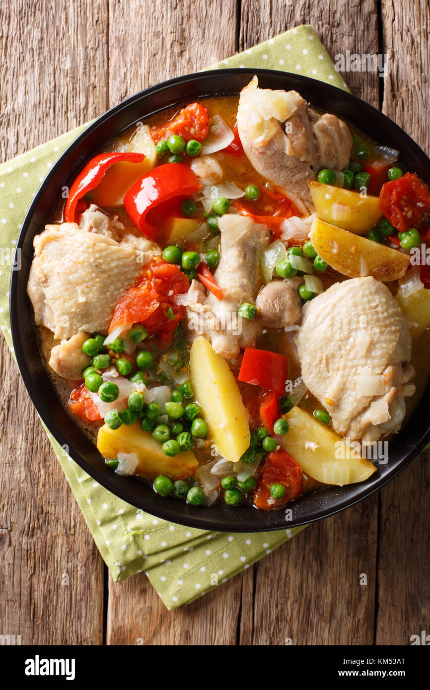 Pieces of chicken stew with potatoes, peppers, tomatoes, peas and onions close-up in a bowl on the table. Vertical top view from above Stock Photo