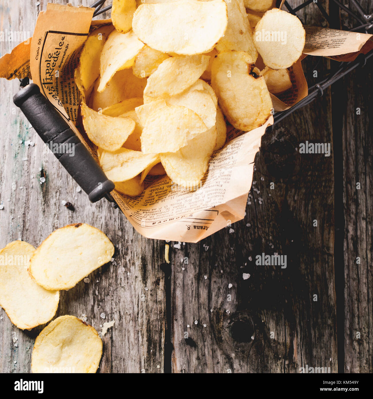 Top view on basket with potato chips with sea salt over old wooden table. Square image Stock Photo