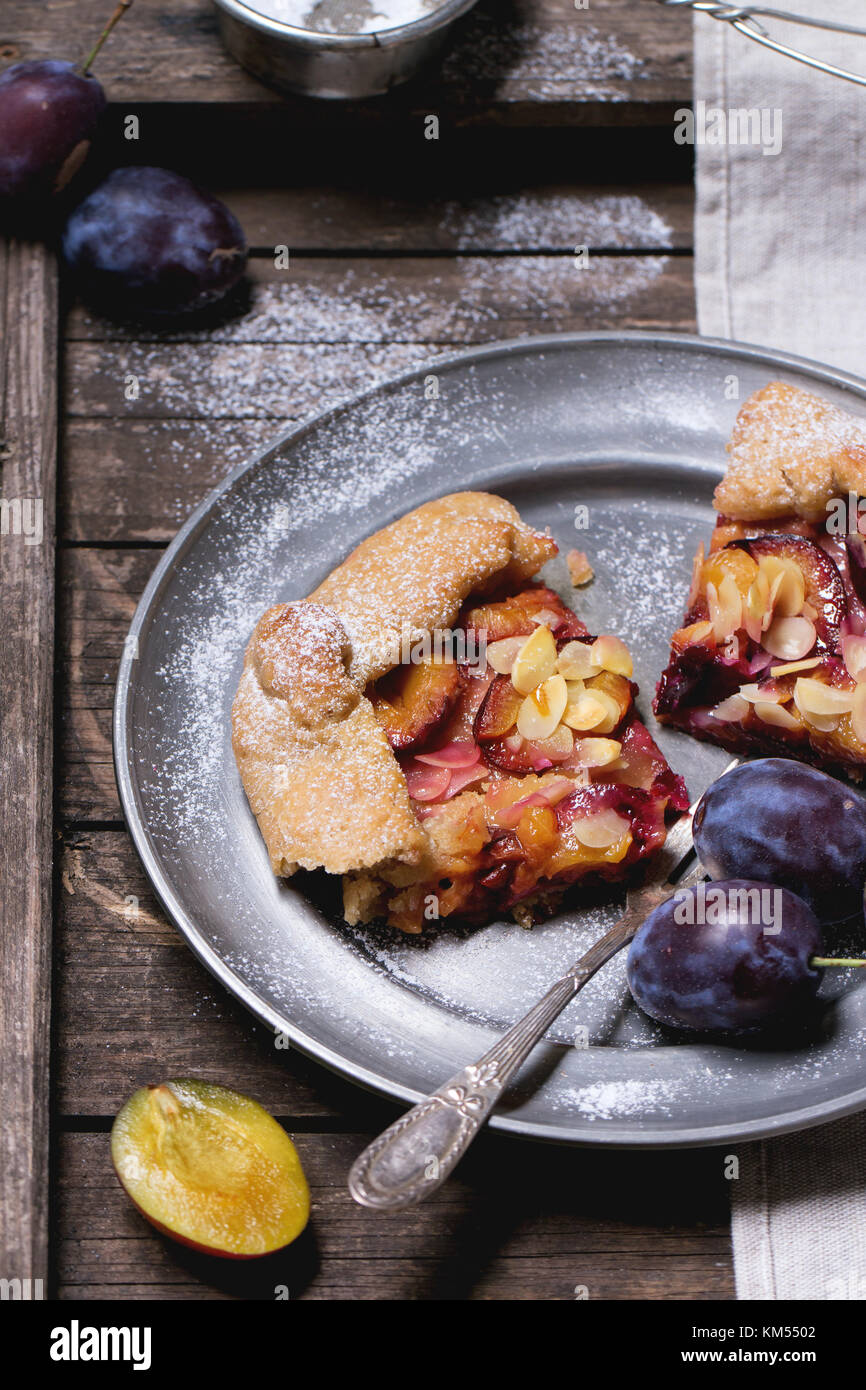 Two pieces of cake galette with plums, served in vintage metal plate over old wooden table. See series Stock Photo