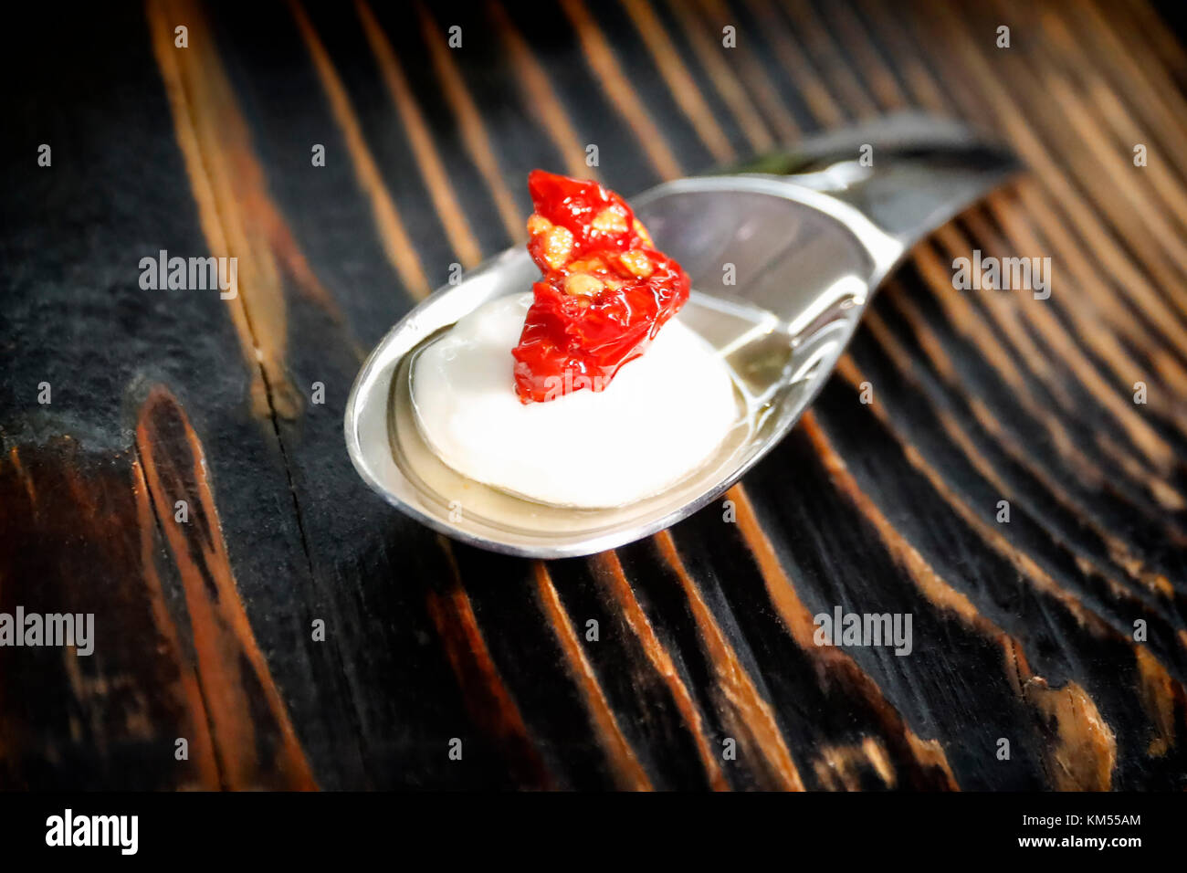 Nibble of mozzarella, served in a teaspoon, with a piece of dried tomato and seed oil on top. Ready to be enjoyed as a small snack Stock Photo