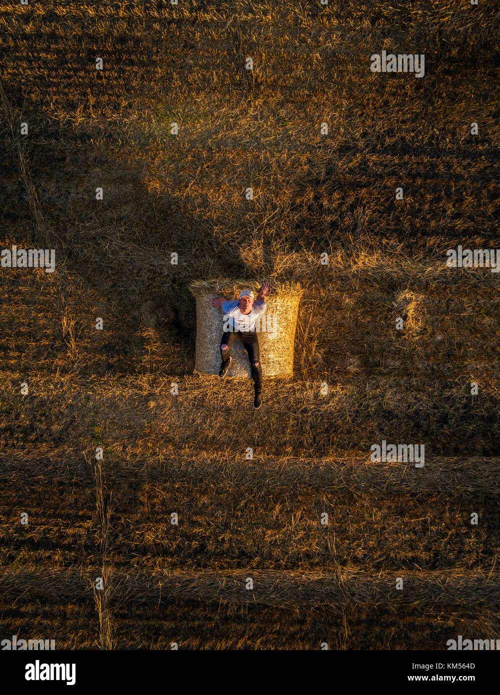 Young man enjoys sunset at the top of a hay bale Stock Photo