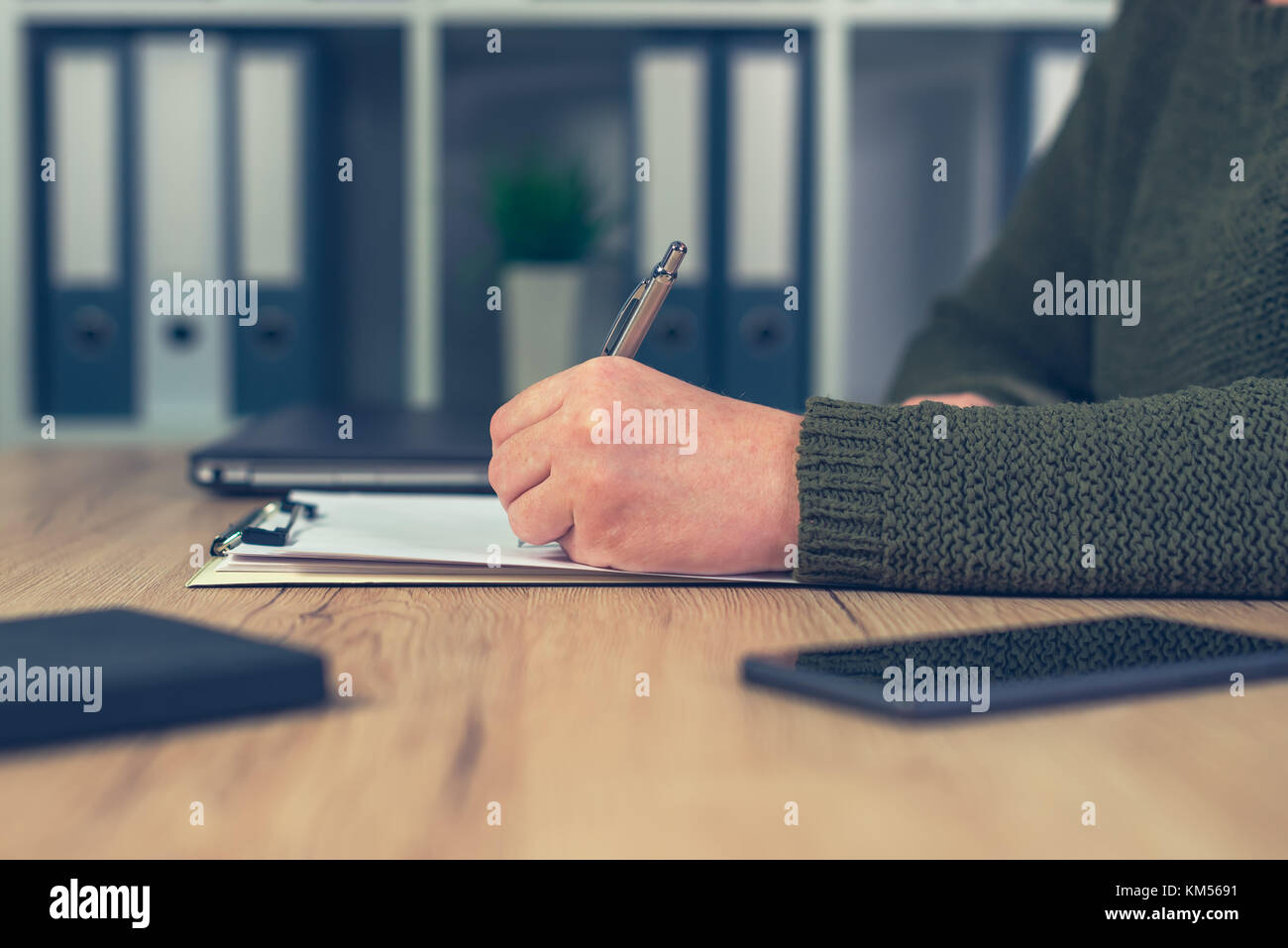 Female business person writing notes on clipboard paper in office Stock Photo