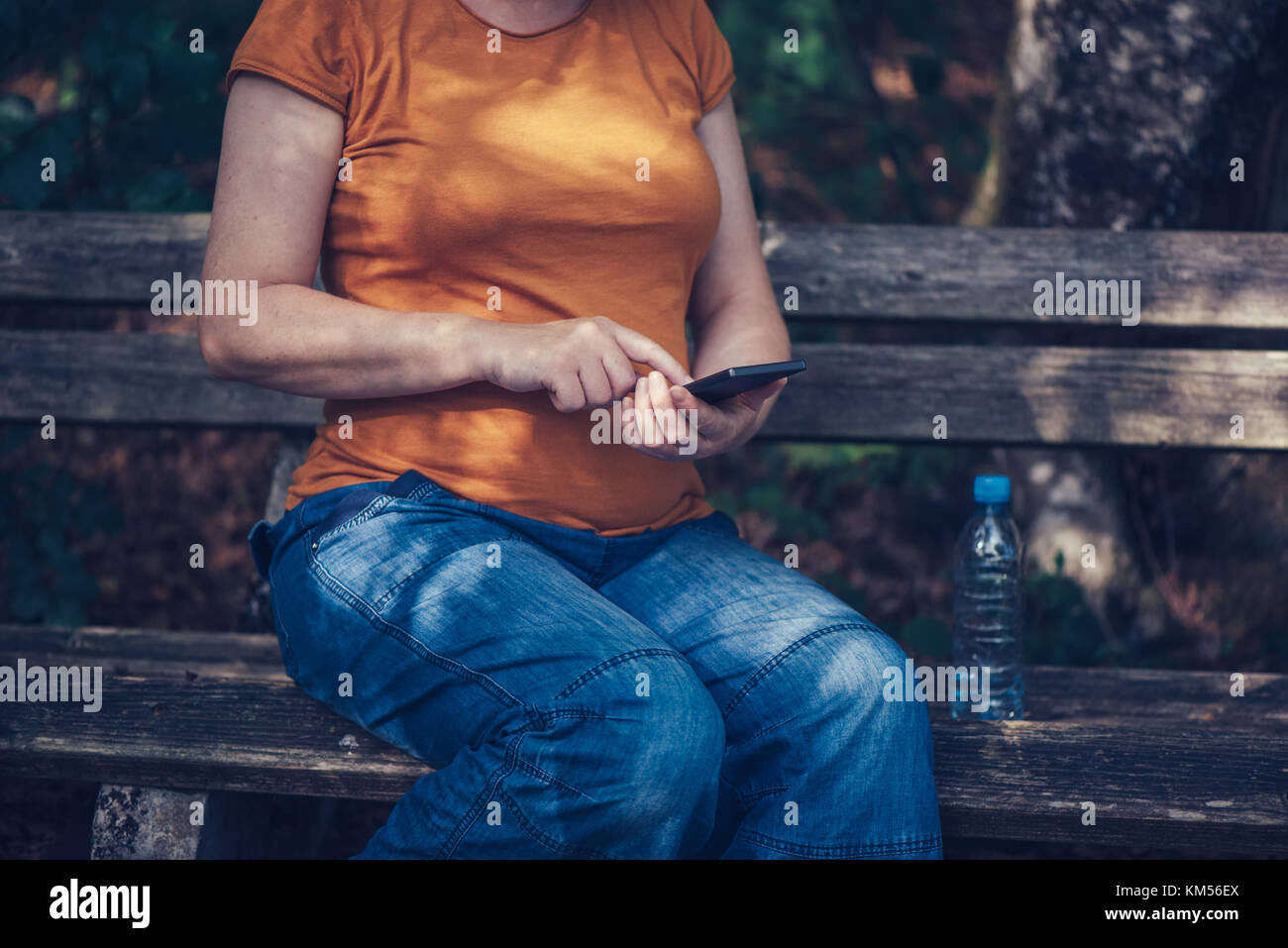Pregnant woman texting outdoors on park bench, adult caucasian female using mobile phone during pregnancy Stock Photo