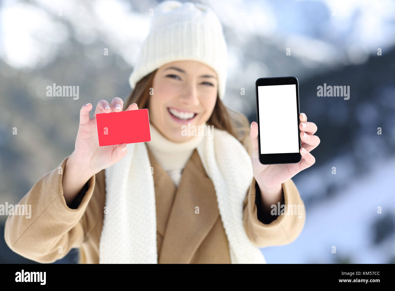 Front view portrait of a woman showing a card and phone screen in a snowy mountain in winter Stock Photo