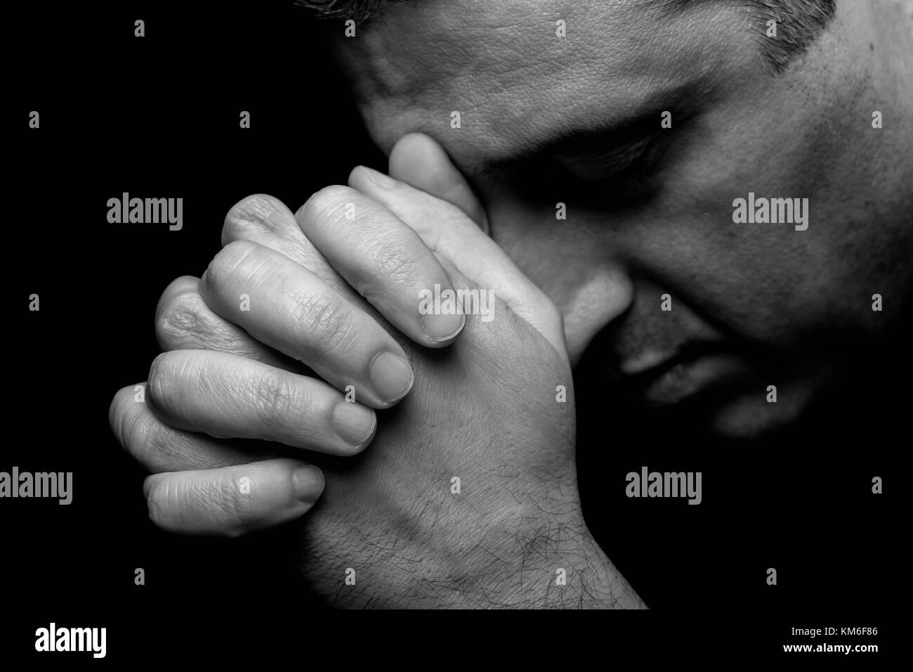 Close up of faithful mature man praying hands folded worship god head down and eyes closed in religious black background religion portrait Christian Stock Photo