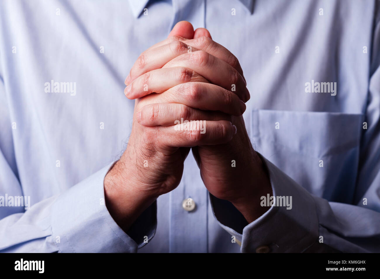Close up or closeup of hands of faithful mature man praying. Hands folded, interlaced fingers in worship to god. Concept for religion, faith, prayer a Stock Photo