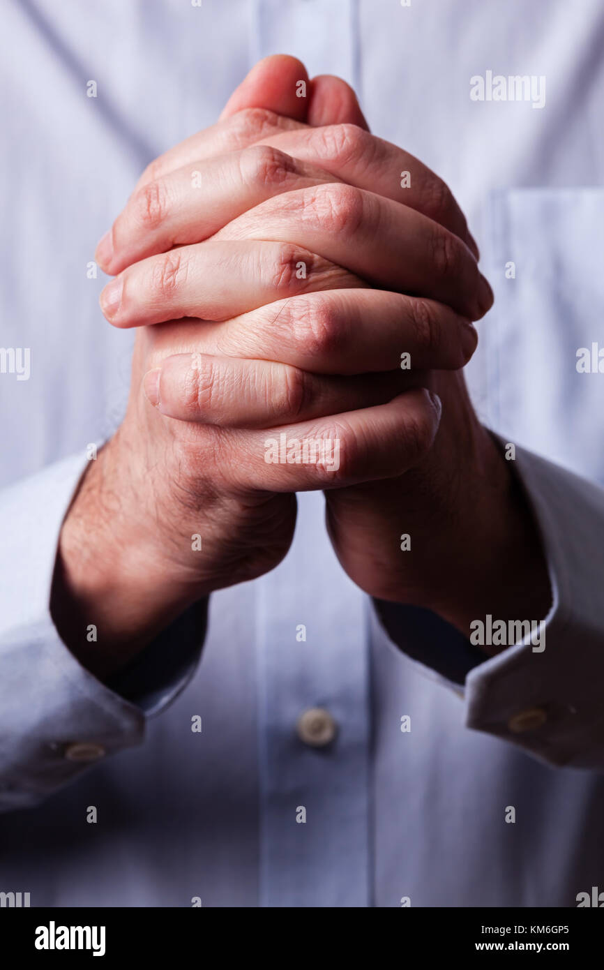 Close up or closeup of hands of faithful mature man praying. Hands folded, interlaced fingers in worship to god. Concept for religion, faith, prayer a Stock Photo