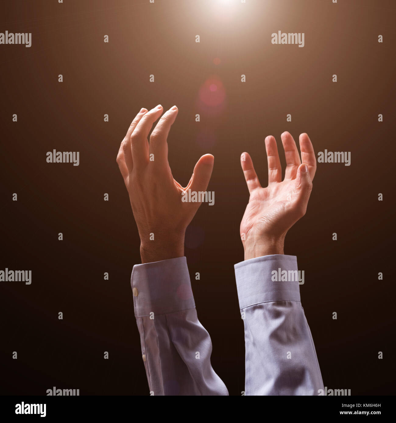 Male arms and hands raised and outstretched in the air to divine light. Man praying, begging, pleading imploring or supplicating. Black background. Stock Photo