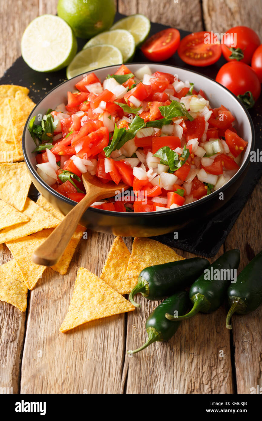 Homemade spicy pico de gallo close-up in a bowl and nachos on the table. vertical Stock Photo