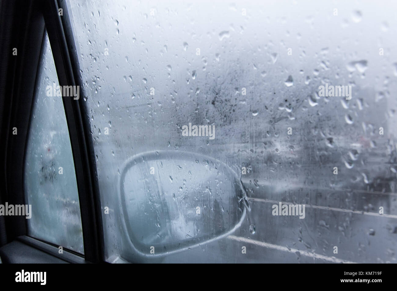 View of a car side mirror from inside the car with condensation and rain on the glass window Stock Photo