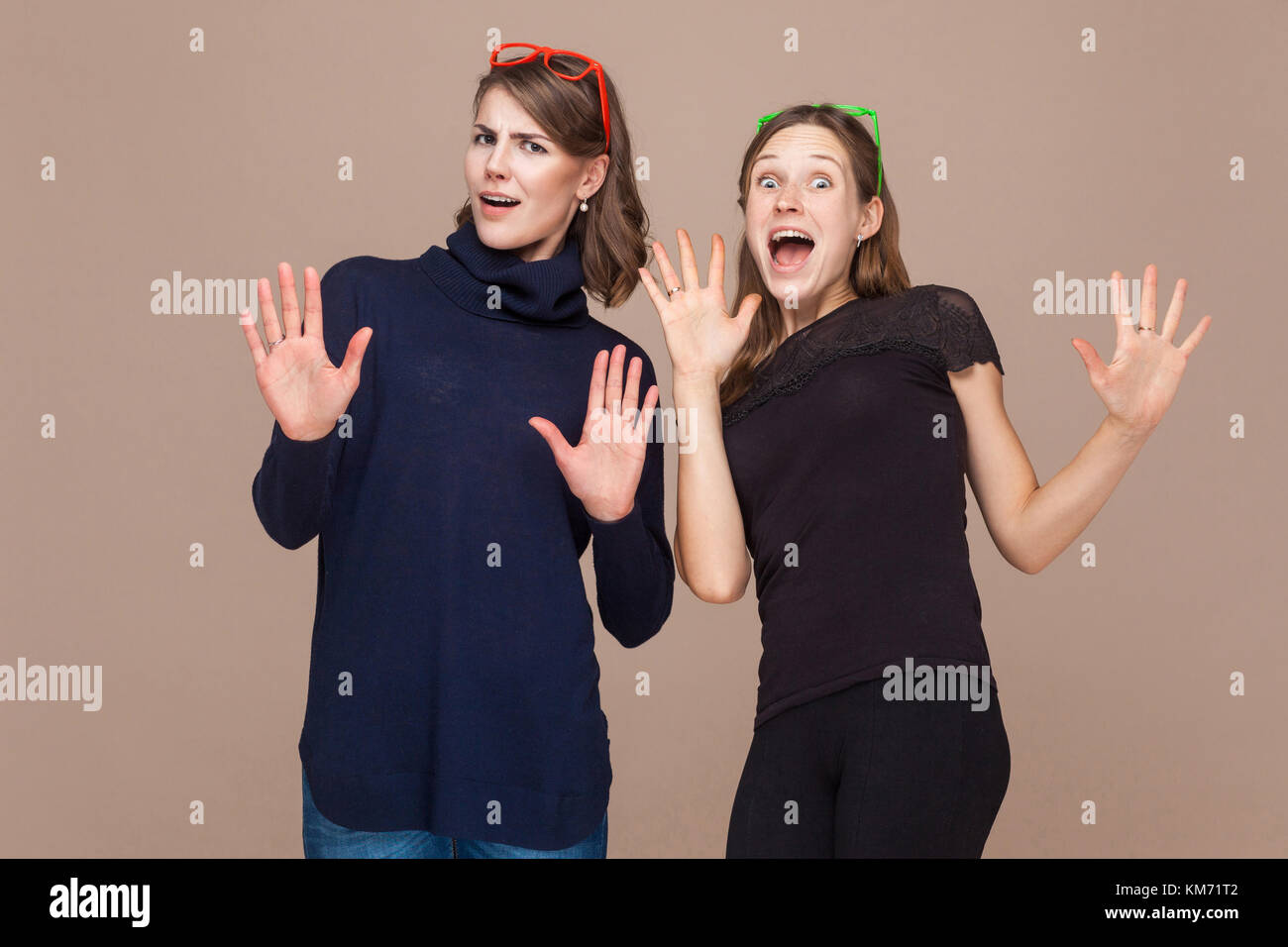 Two sisters standing near each other and amazement. Studio shot, light brown background Stock Photo