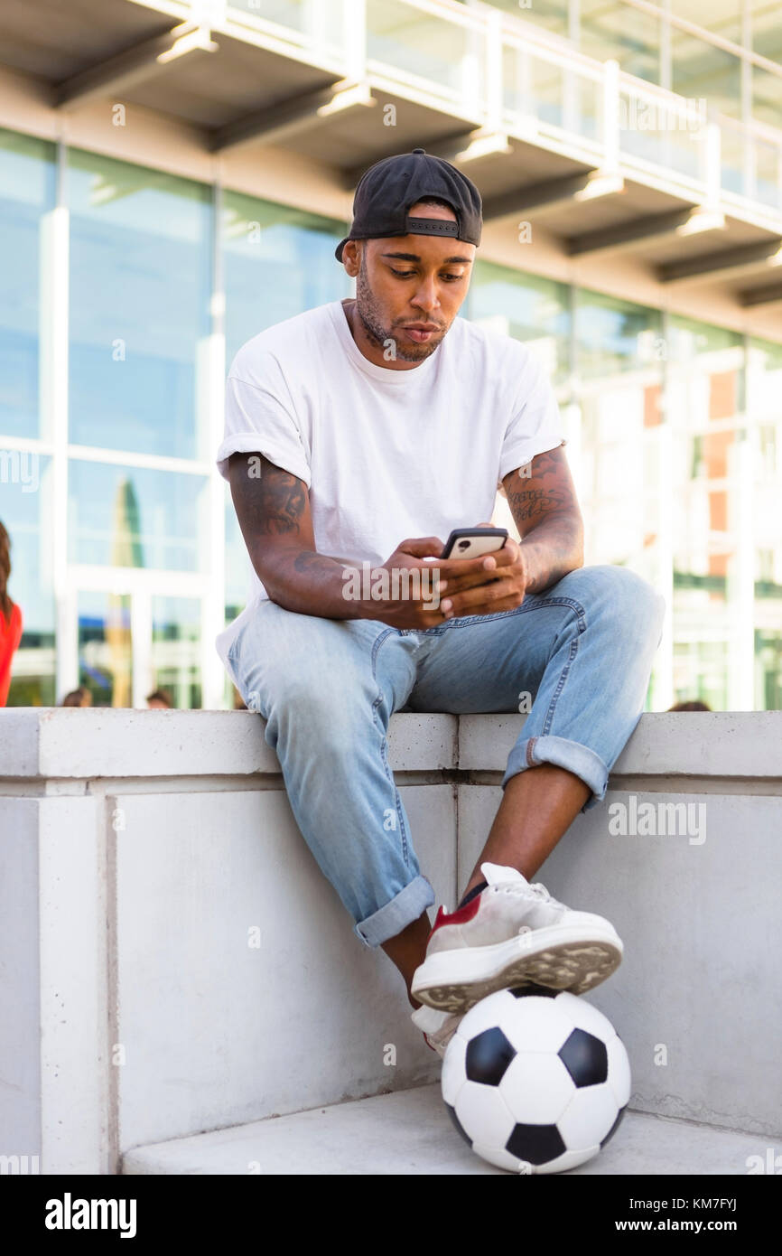 Young man with soccer ball and cell phone in urban area Stock Photo