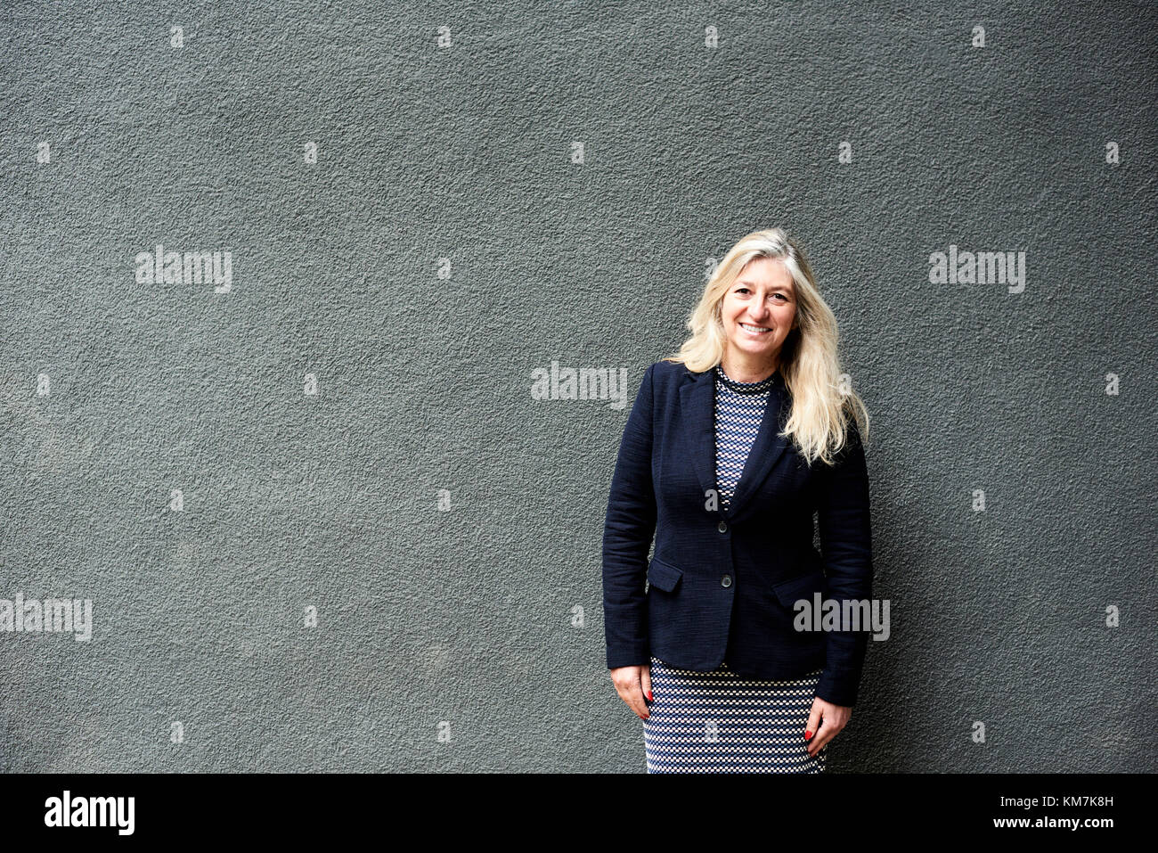 London, UK, grey haired senior business woman smiling at camera against a grey wall, senior business women Stock Photo