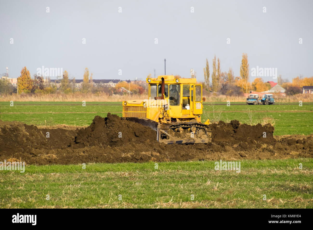 The yellow tractor with attached grederom makes ground leveling. Work on the drainage system in the field. Stock Photo