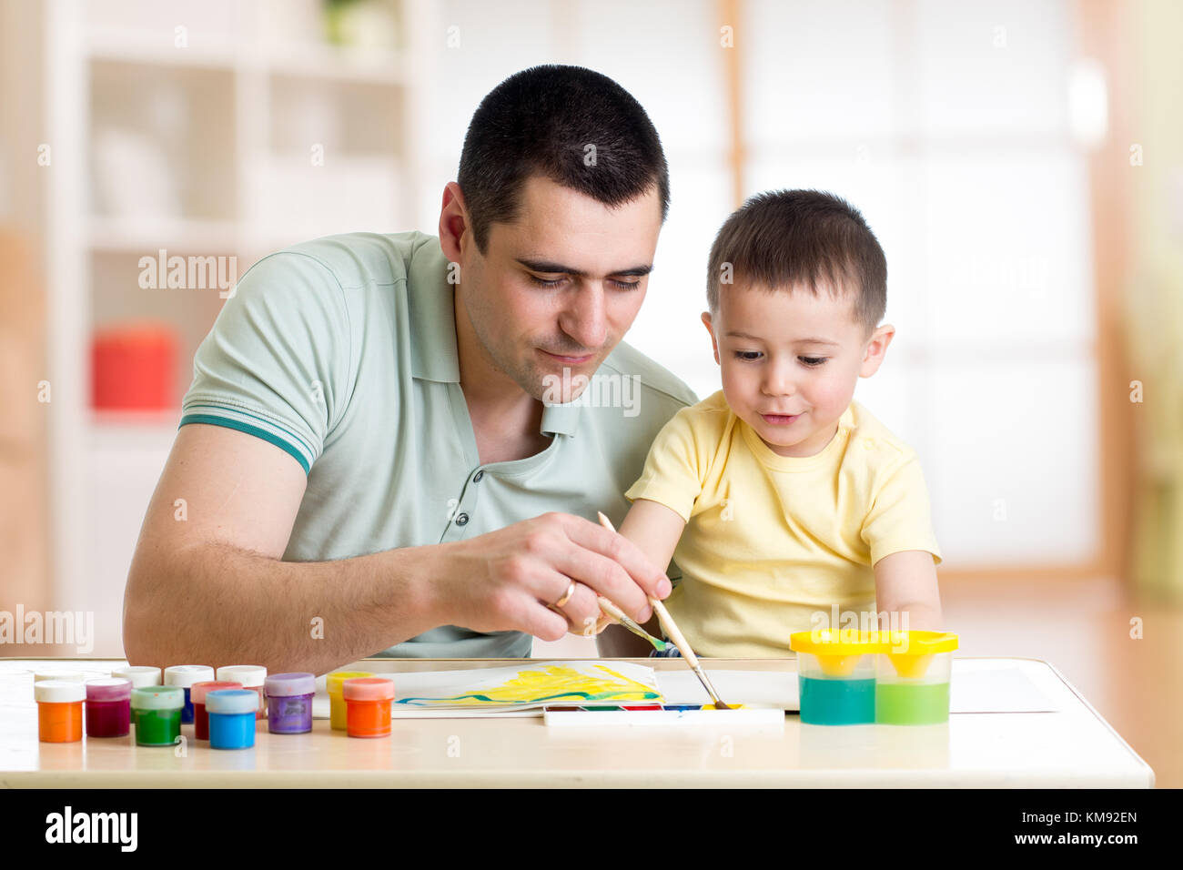 Father and son are painting together. Happy family are coloring with paintbrush. Man and child have a fun pastime. Stock Photo