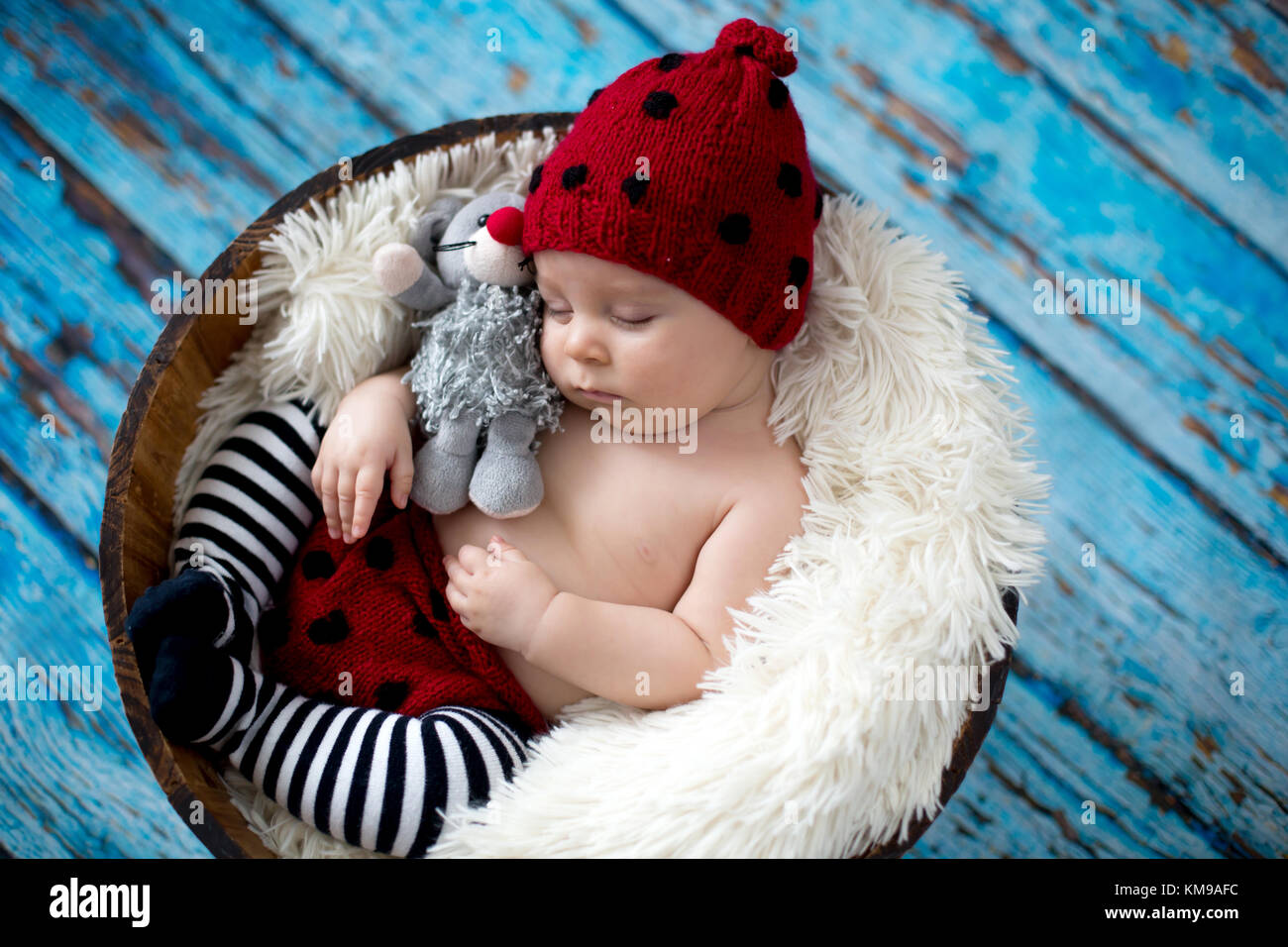 Little baby boy with knitted ladybug hat and pants in a basket, sleeping peacefully in a basket, isolated studio shot Stock Photo