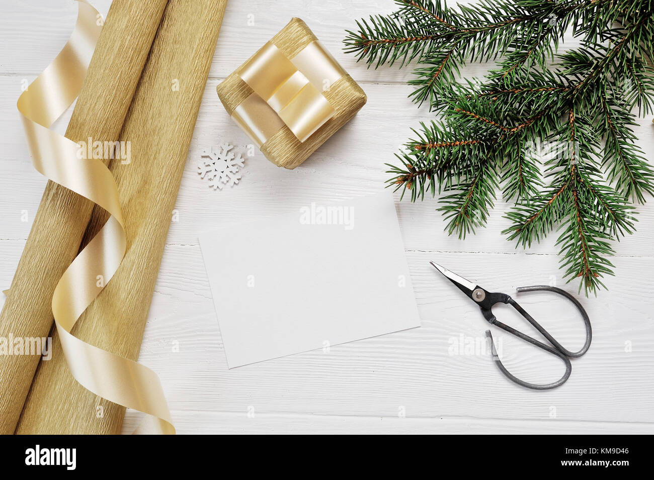 Mockup Christmas decor top view Packing paper and gold gift ribbon and scissors, flatlay on a white wooden background, with place for your text Stock Photo