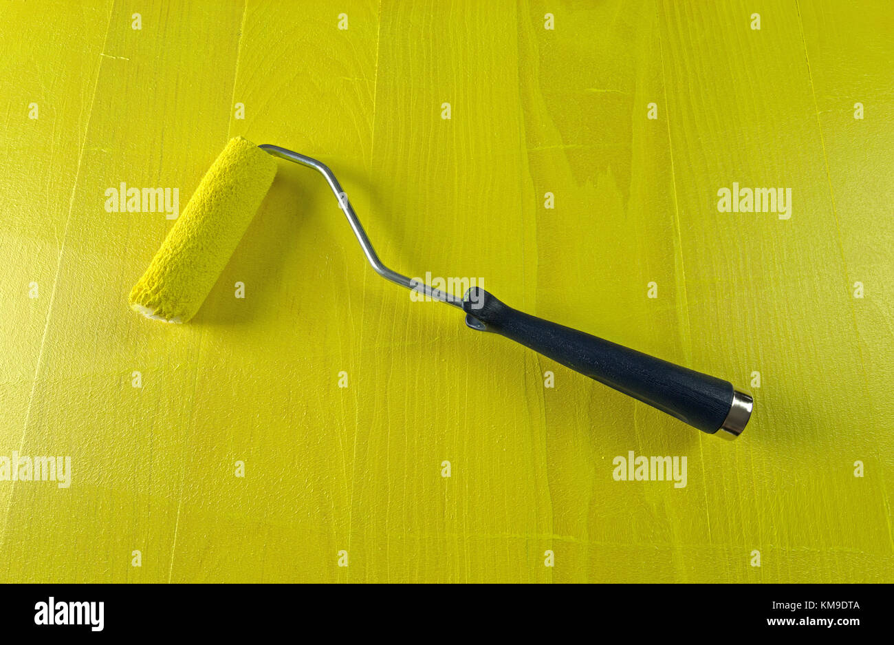 A saturated smooth texture paint roller atop bright yellow painted pine wood. Stock Photo