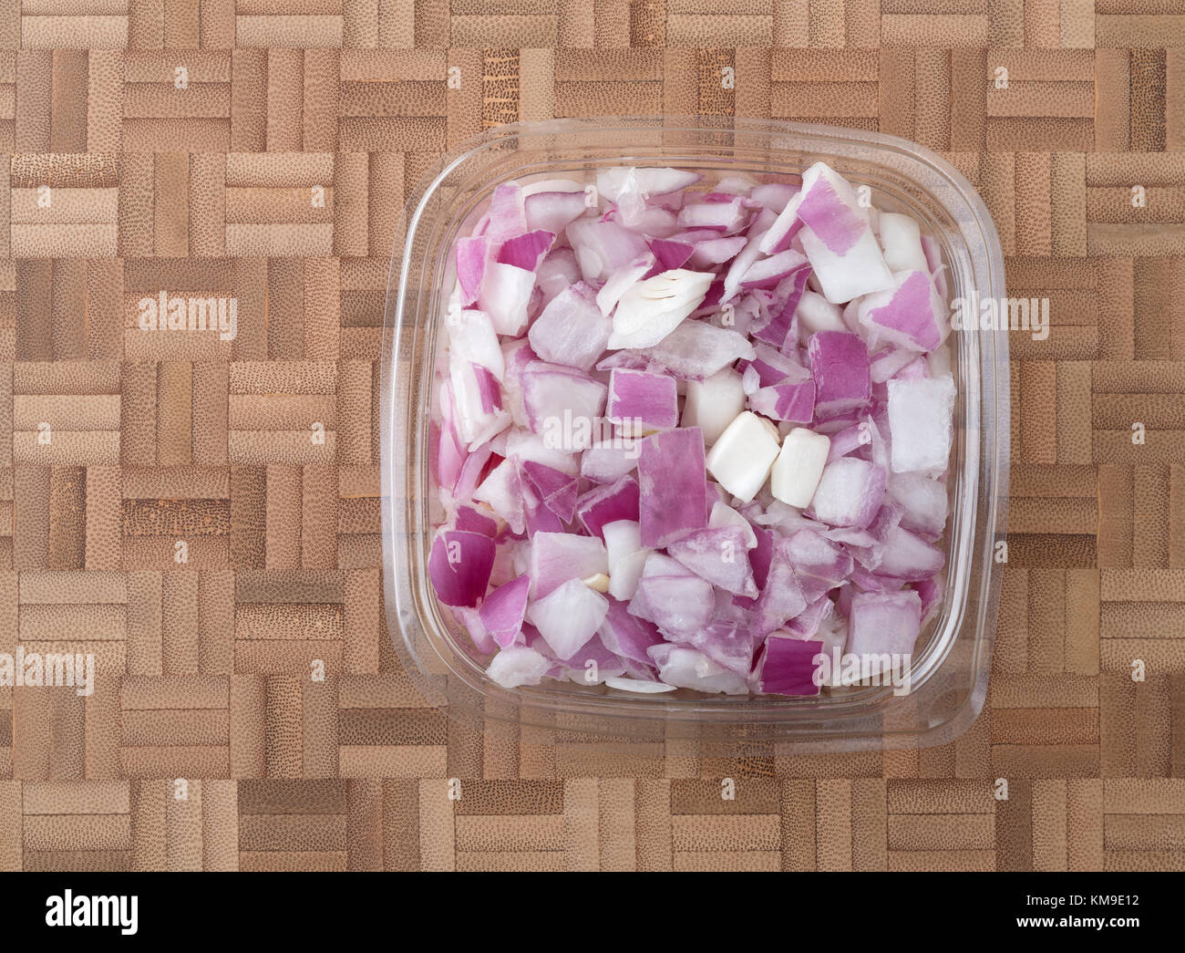 Top view of a small plastic container of freshly chopped red onions on a wood bamboo cutting
