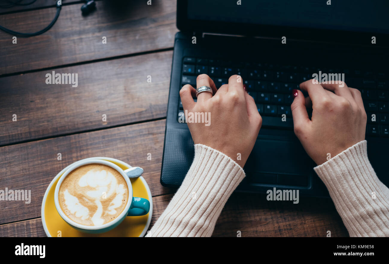 Cup of coffee next to a woman using laptop Stock Photo