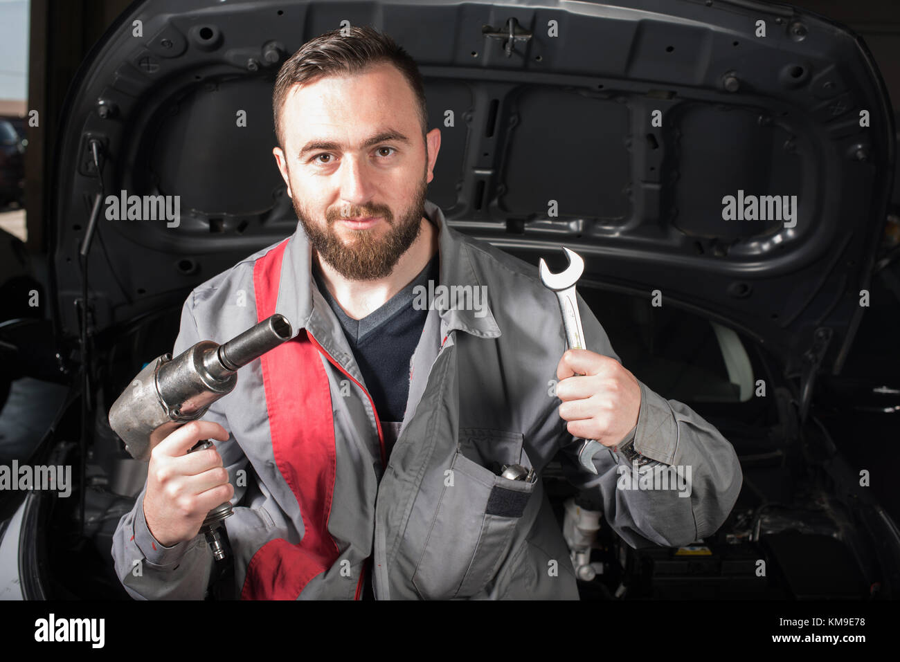 Mechanic standing by a car holding tools Stock Photo