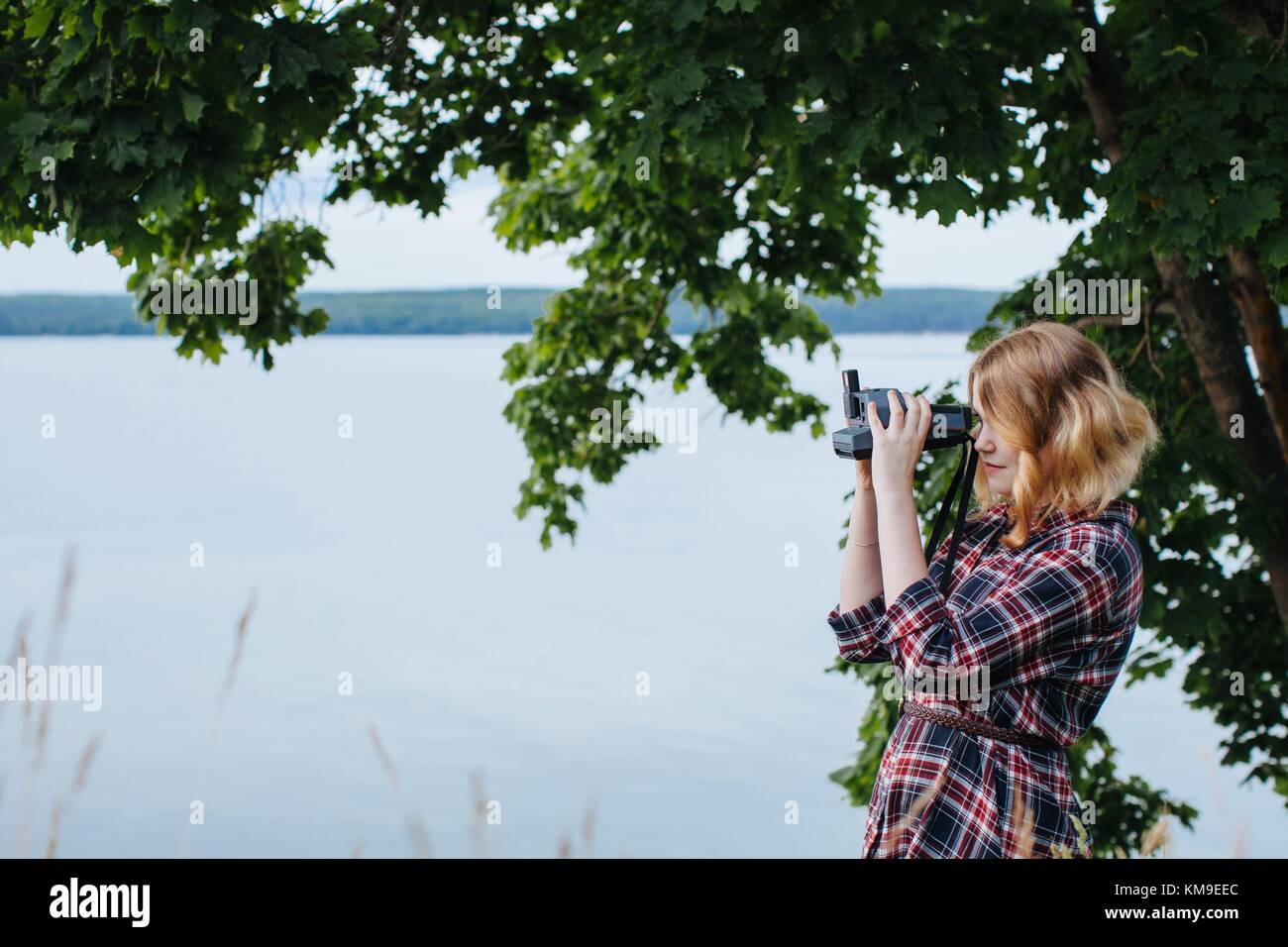 Woman standing by river taking a photo with an instant camera Stock ...