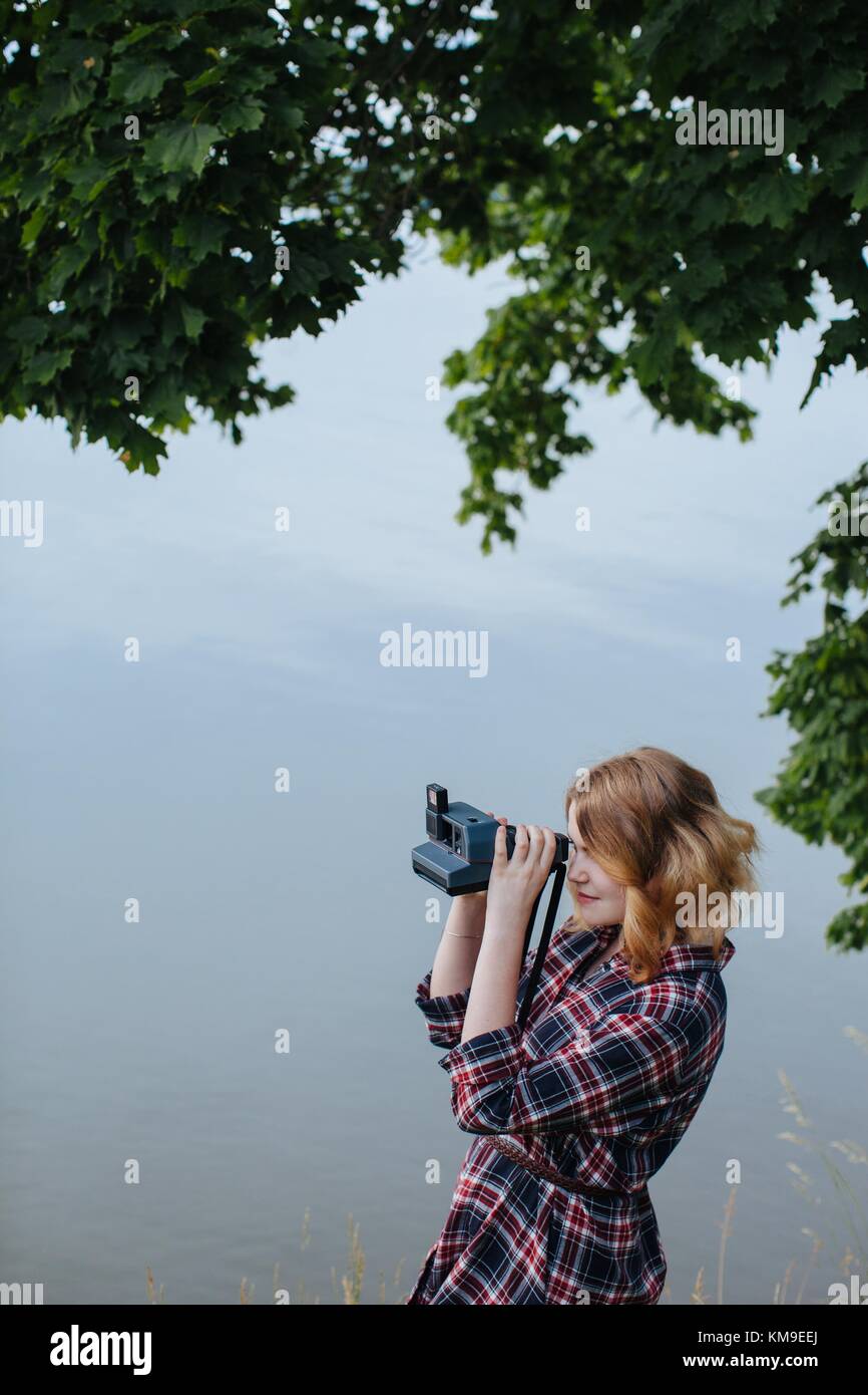 Woman standing by river taking a photo with an instant camera Stock ...