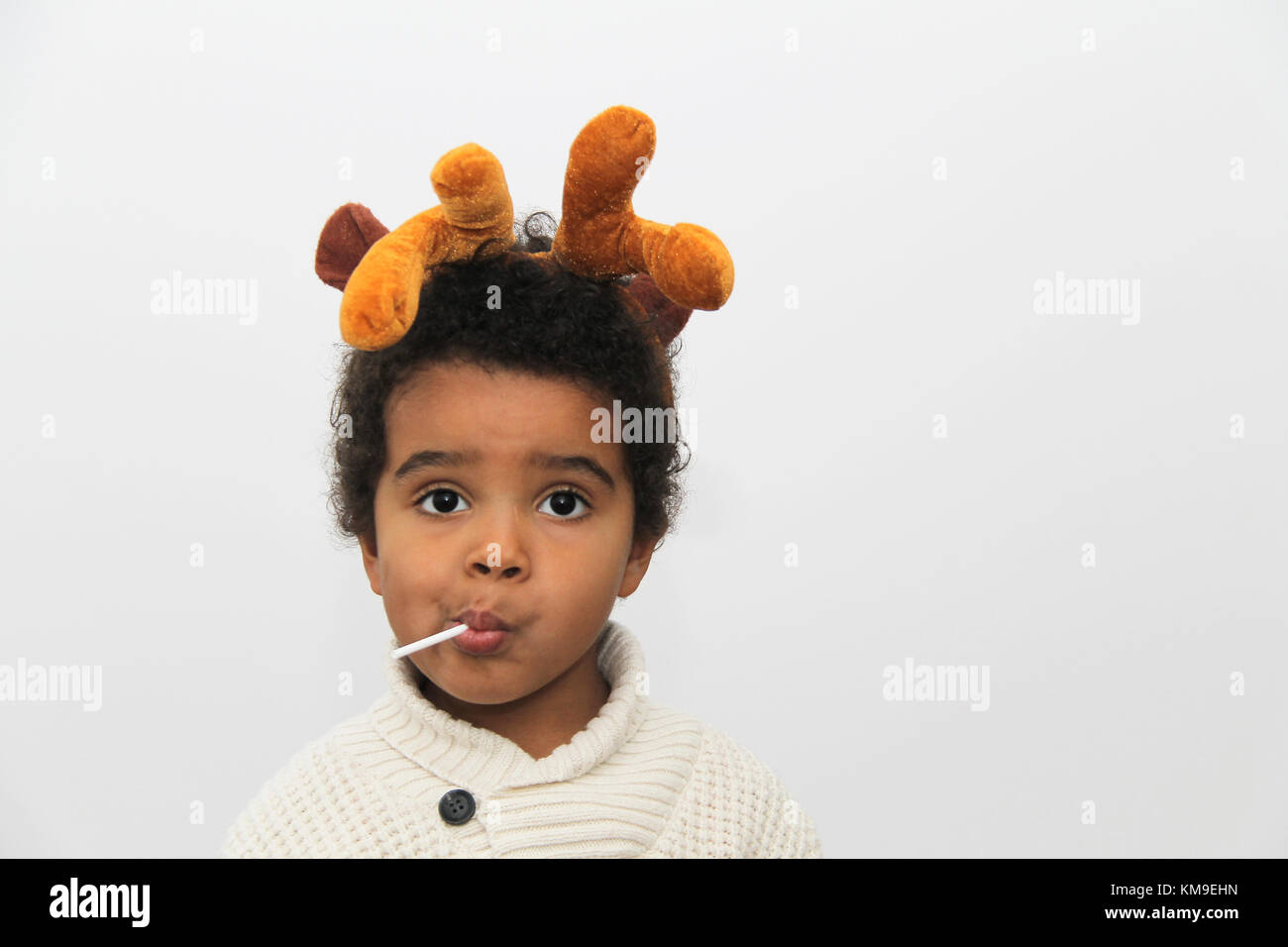 Portrait of a smiling boy wearing Christmas antlers eating a lollipop Stock Photo