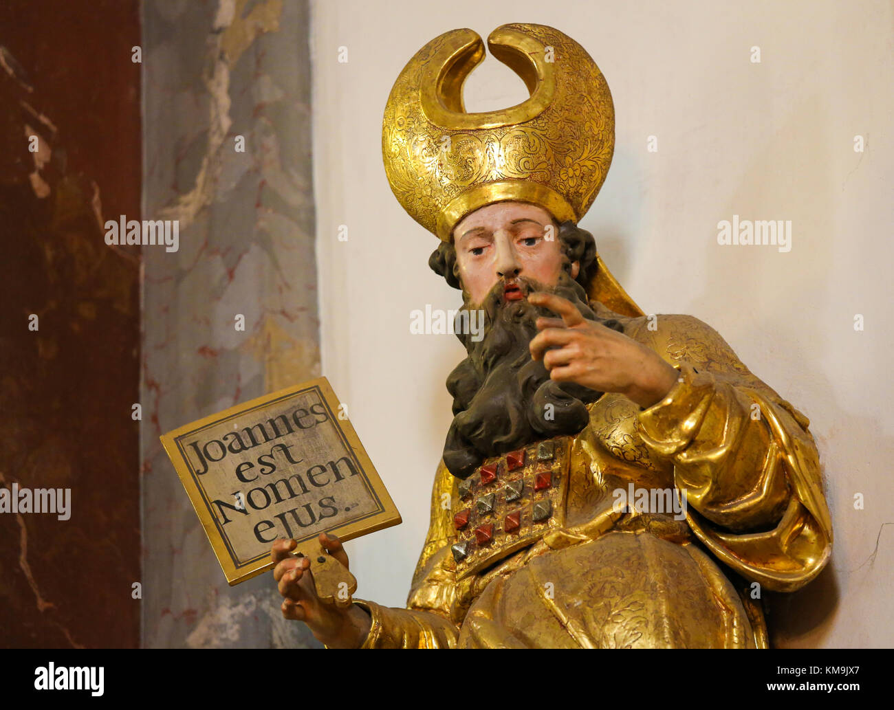 Statue of a Saint holding a sign with the Latin text Joannes est Nomen Ejus or John is his name, refering to St John the Baptist, in Loreta Church in  Stock Photo