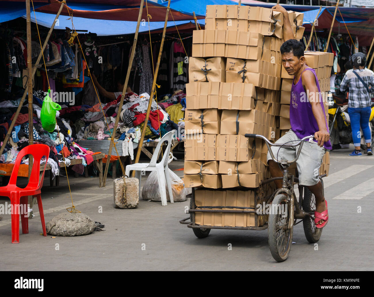 A man balances a large load of cardboard boxes stacked on a Trisikad