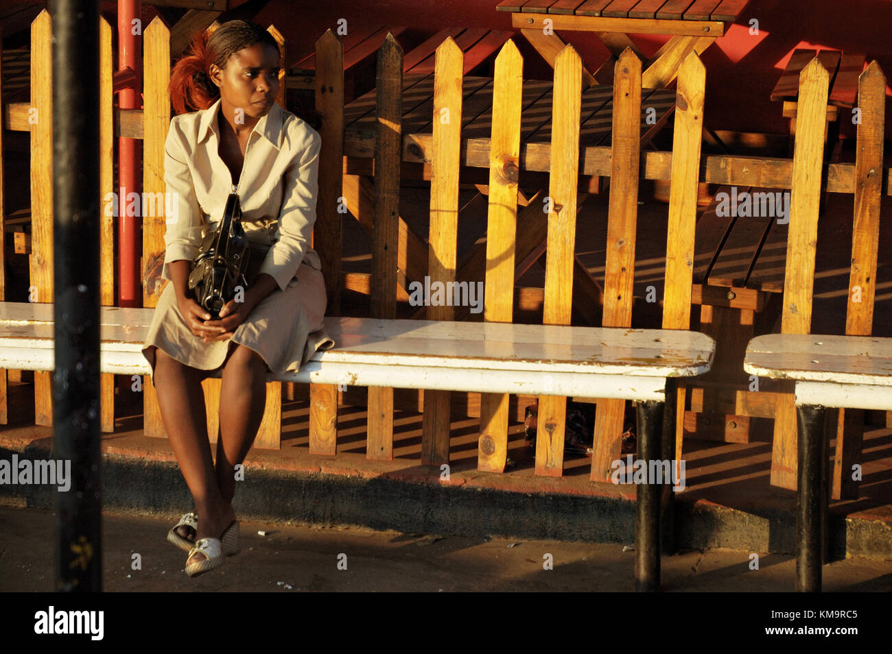 Young Zambian woman sitting on a bench and waiting the bus in Livingstone, Southern Province, Zambia Stock Photo