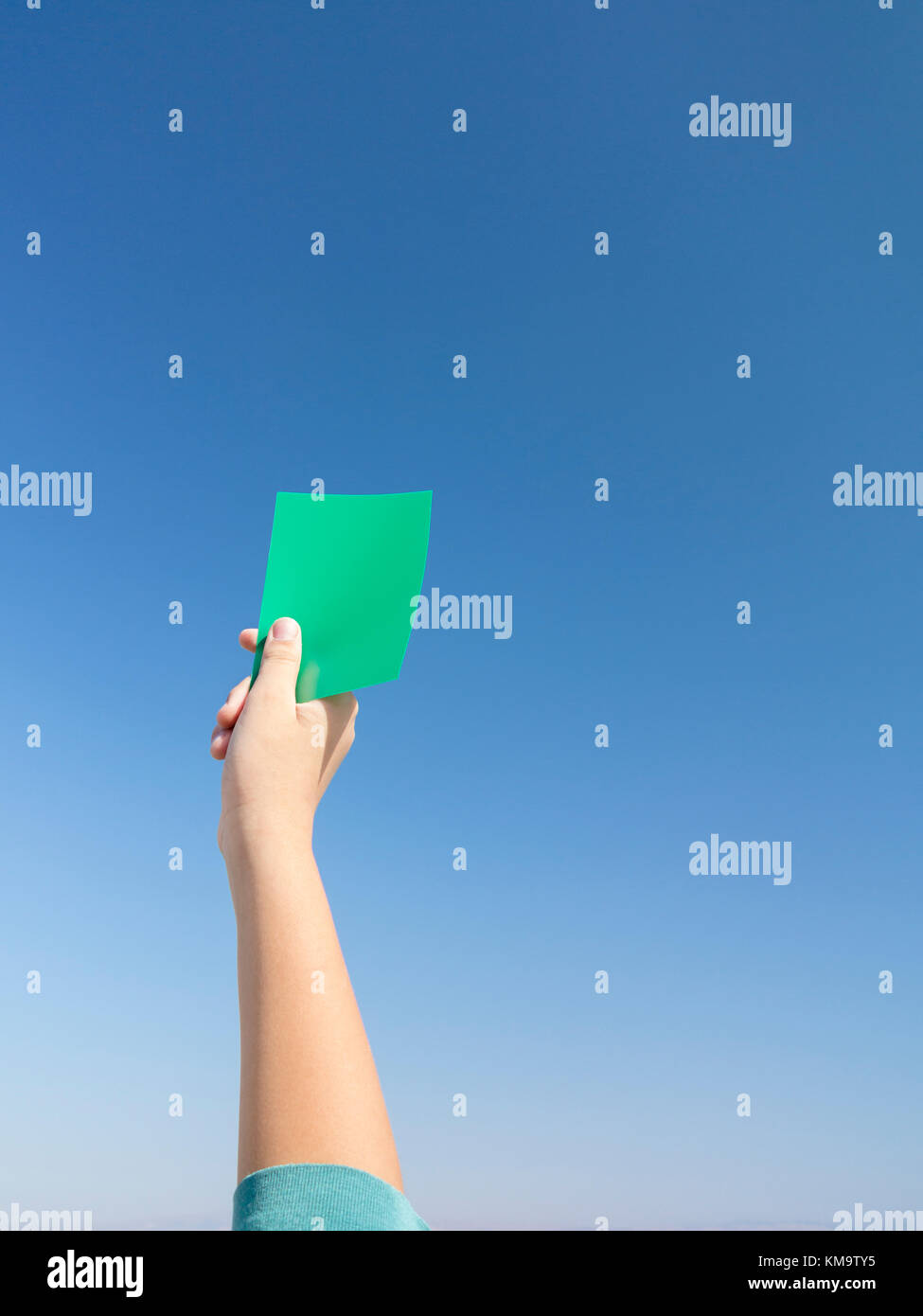 Hand holding green card against blue sky Stock Photo