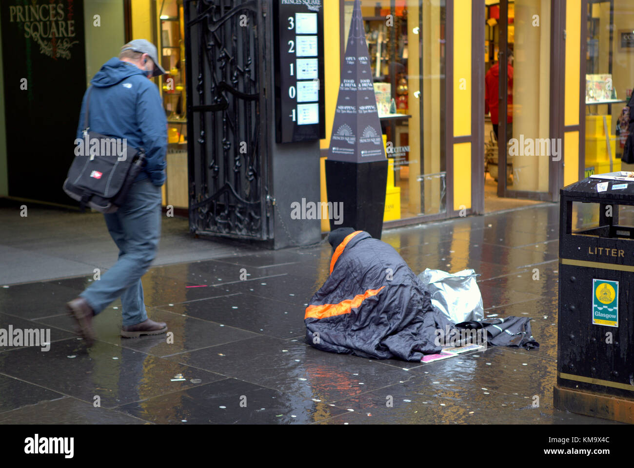 homeless man in a sleeping bag on buchanan  street on the style mile with possessions begging in front of the upmarket princes square shopping centre Stock Photo