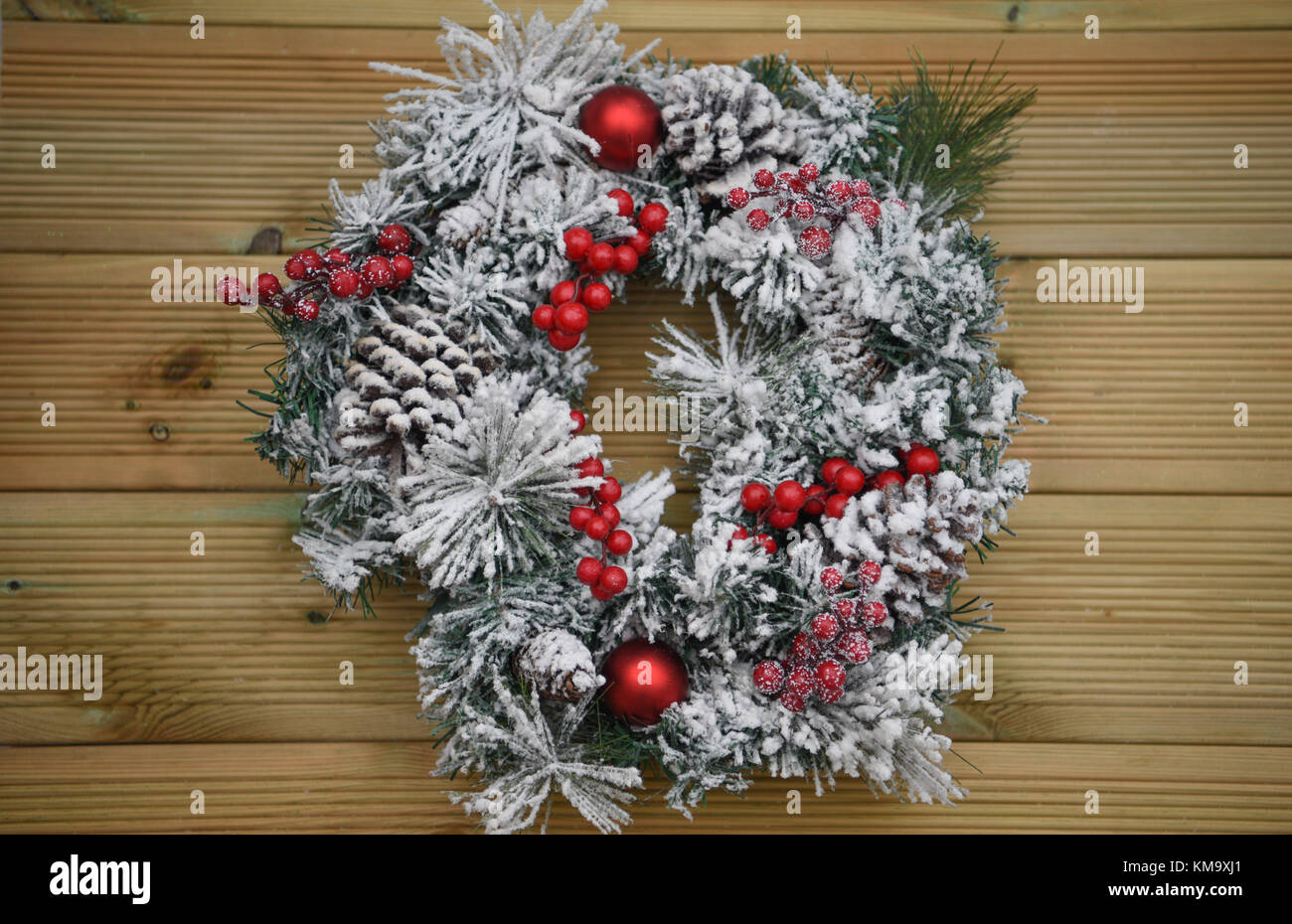 Christmas photography image of a green pine tree wreath covered in snow with red berries and on rustic natural wood background Stock Photo